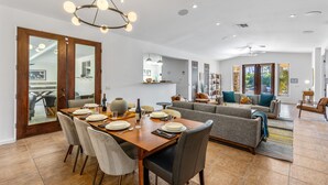 A spacious living area with a dining table set for four, a grey sofa, and a chandelier. - Mirador Desert Oasis – Mediterranean Escape (Palm Springs)