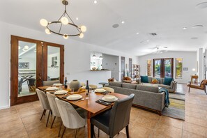 A spacious living area with a dining table set for four, a grey sofa, and a chandelier.