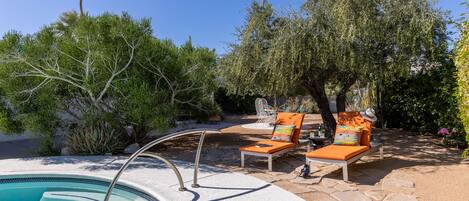 A pool area with lounge chairs, a stone pathway, and surrounding vegetation.