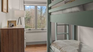 A bunk bed with a view of trees, a wooden dresser, a lamp, and a patterned rug. - 2BR Stowe Mountain Unit | River & Ski Access (Stowe)