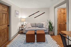 A cozy living room with a grey sofa, two brown ottomans, a wooden table, and a potted plant.