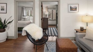 A modern living room with a sofa, a chair, a lamp, and a rug. There is a bed in the adjacent room. - 2BR Stowe Mountain Unit | River & Ski Access (Stowe)