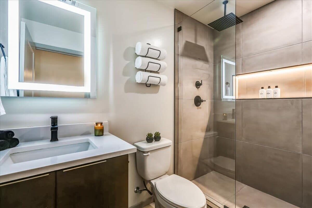 Une salle de bain moderne avec un lavabo, des toilettes et une douche. On y trouve des articles de toilette accrochés au mur et un miroir au-dessus du lavabo.
