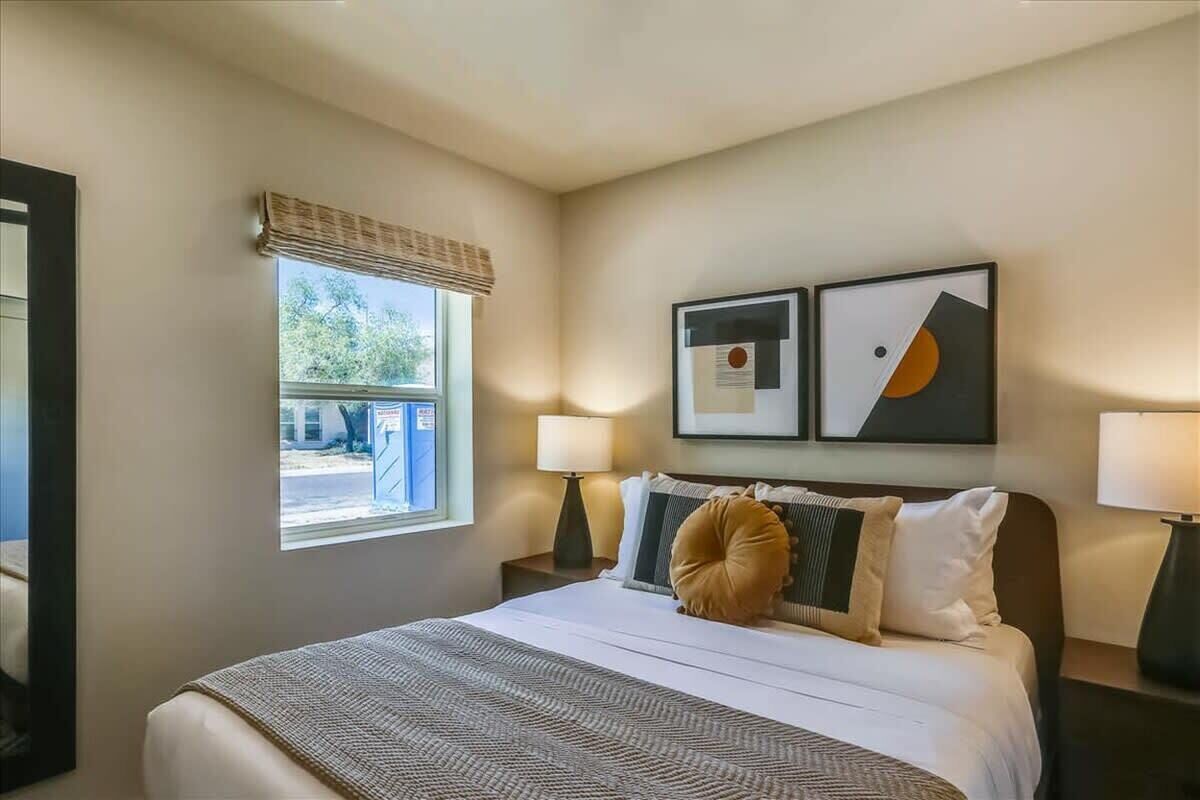 Une chambre d’hôtel avec un lit, deux lampes de chevet, une fenêtre donnant sur un beau paysage et deux tableaux encadrés au mur.