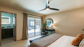 Ein Hotelzimmer mit Bett, Schreibtisch, Stuhl, Deckenventilator, einem großen Fenster mit Vorhängen und Blick ins Freie.