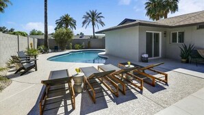 Ein Garten mit Schwimmbad, Liegestühlen und Palmen.