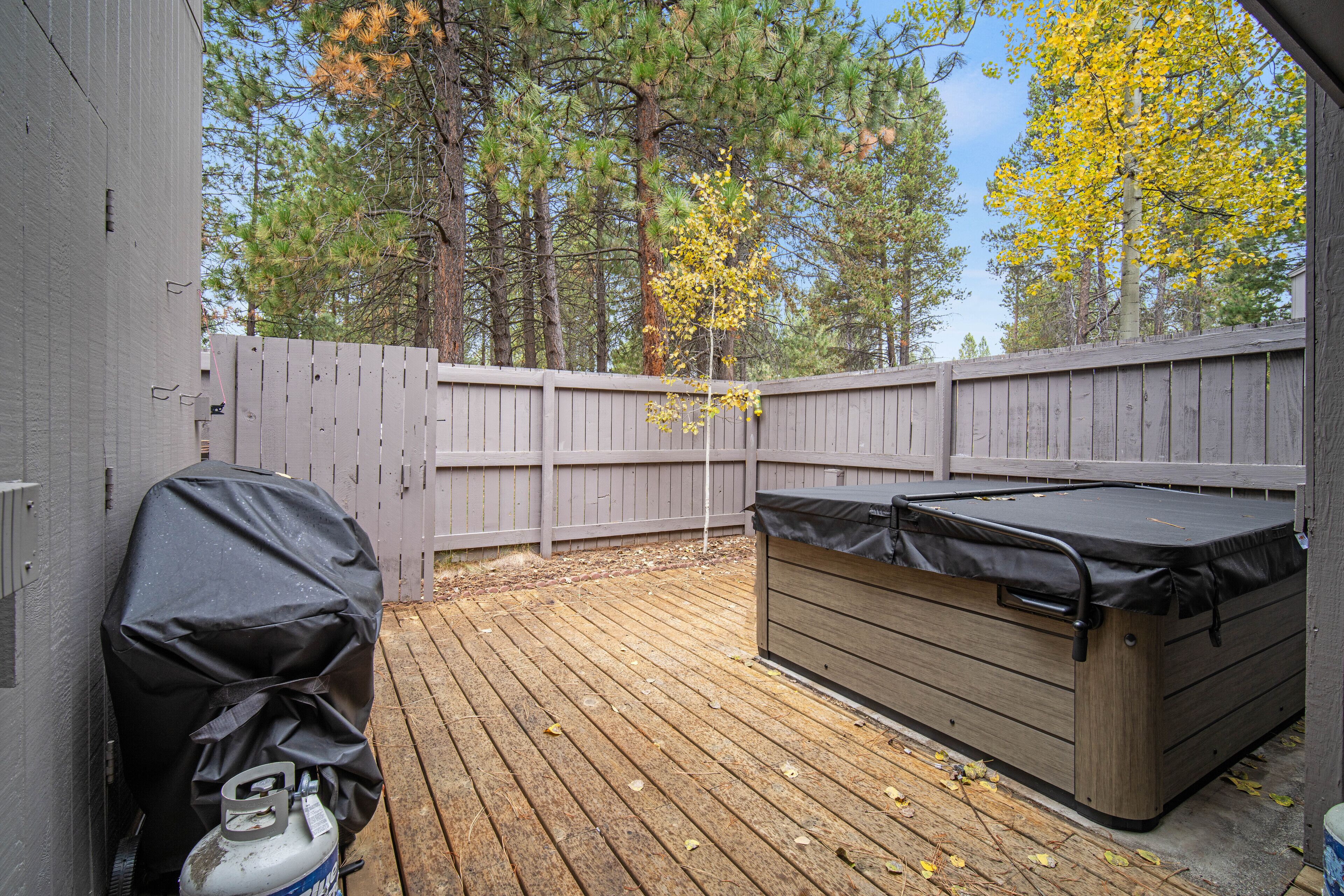 A backyard with a wooden deck, a covered grill, and a hot tub.