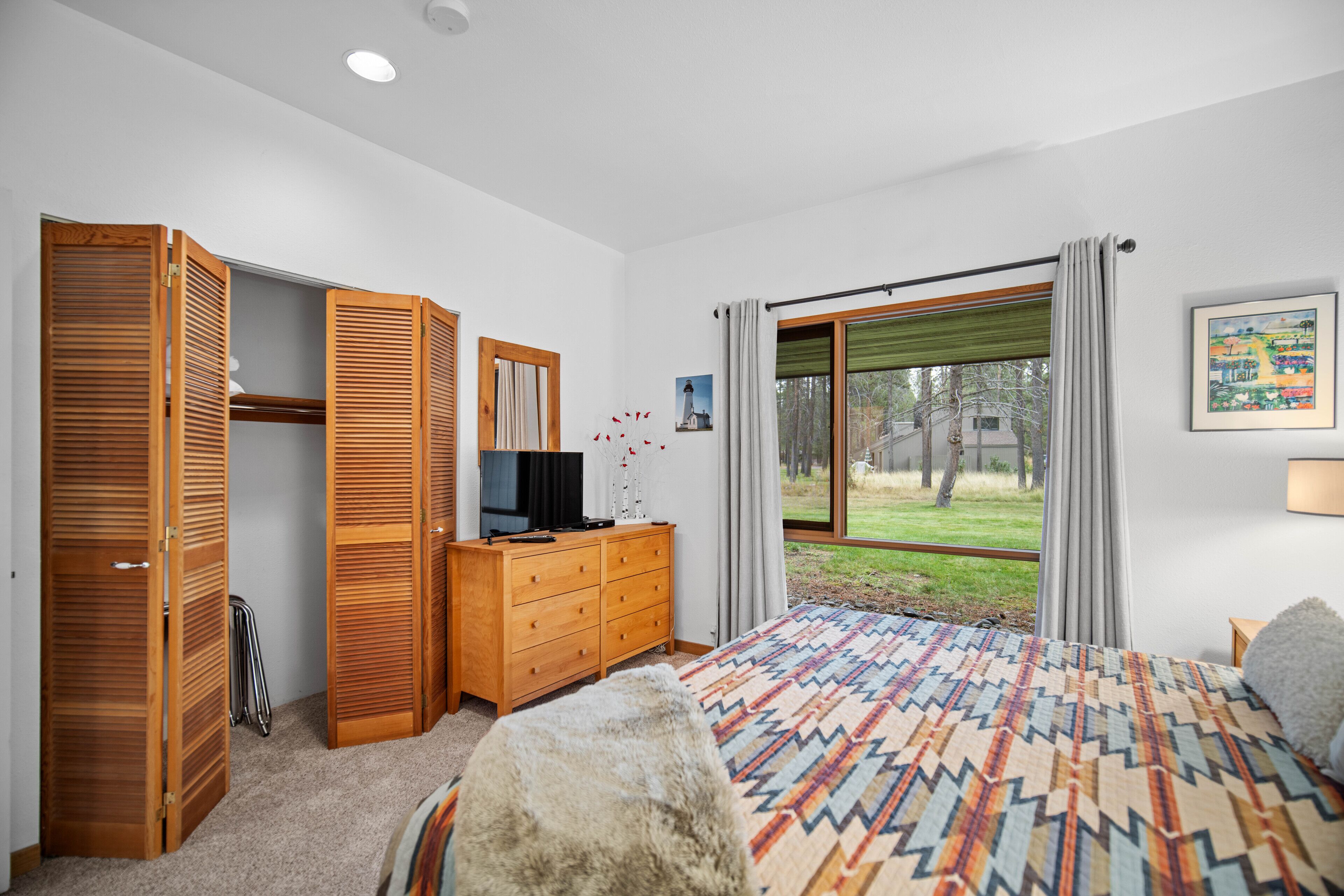A bedroom with a bed, wooden wardrobe, a dresser, a television, and a window with curtains.