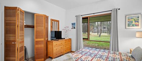 A bedroom with a bed, wooden wardrobe, a dresser, a television, and a window with curtains.
