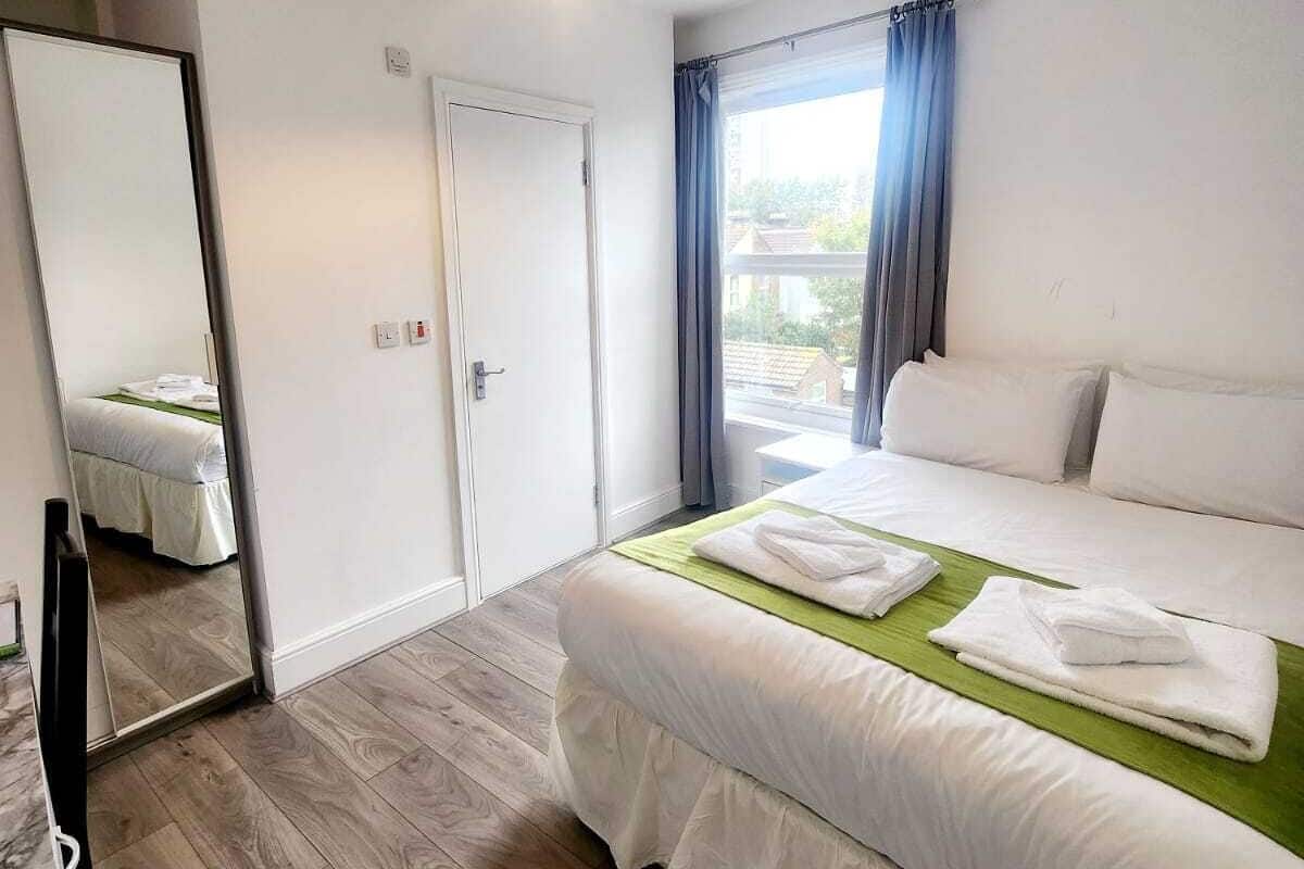 A hotel room with a bed, a mirror, a door, and a window with curtains.