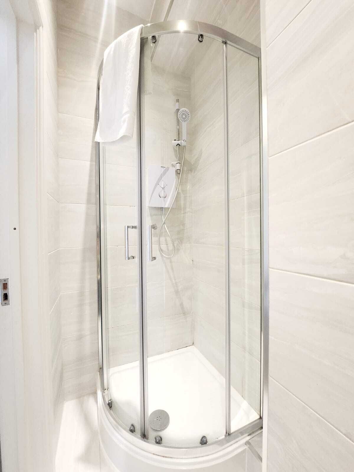Ducha envuelta en vidrio con cabezal de ducha de mano y panel de control.