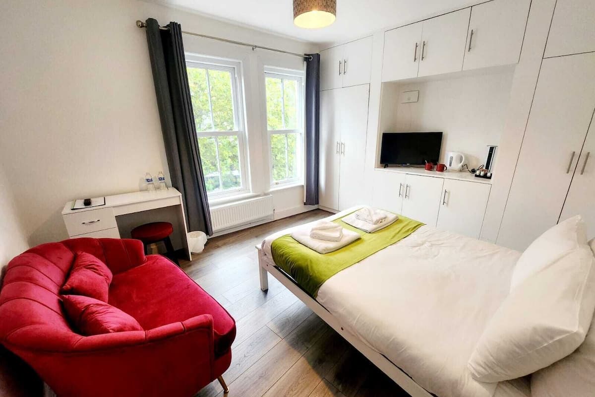 A bedroom with a bed, a desk, a red chair, and a TV.