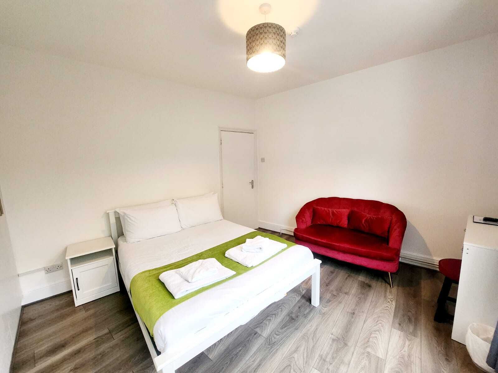 Un dormitorio con una cama, una silla roja, un armario blanco y un mueble pequeño blanco.