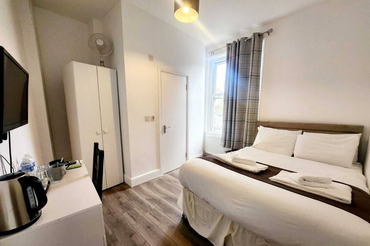 A hotel room with a bed, a desk with a kettle, a wardrobe, and a television.