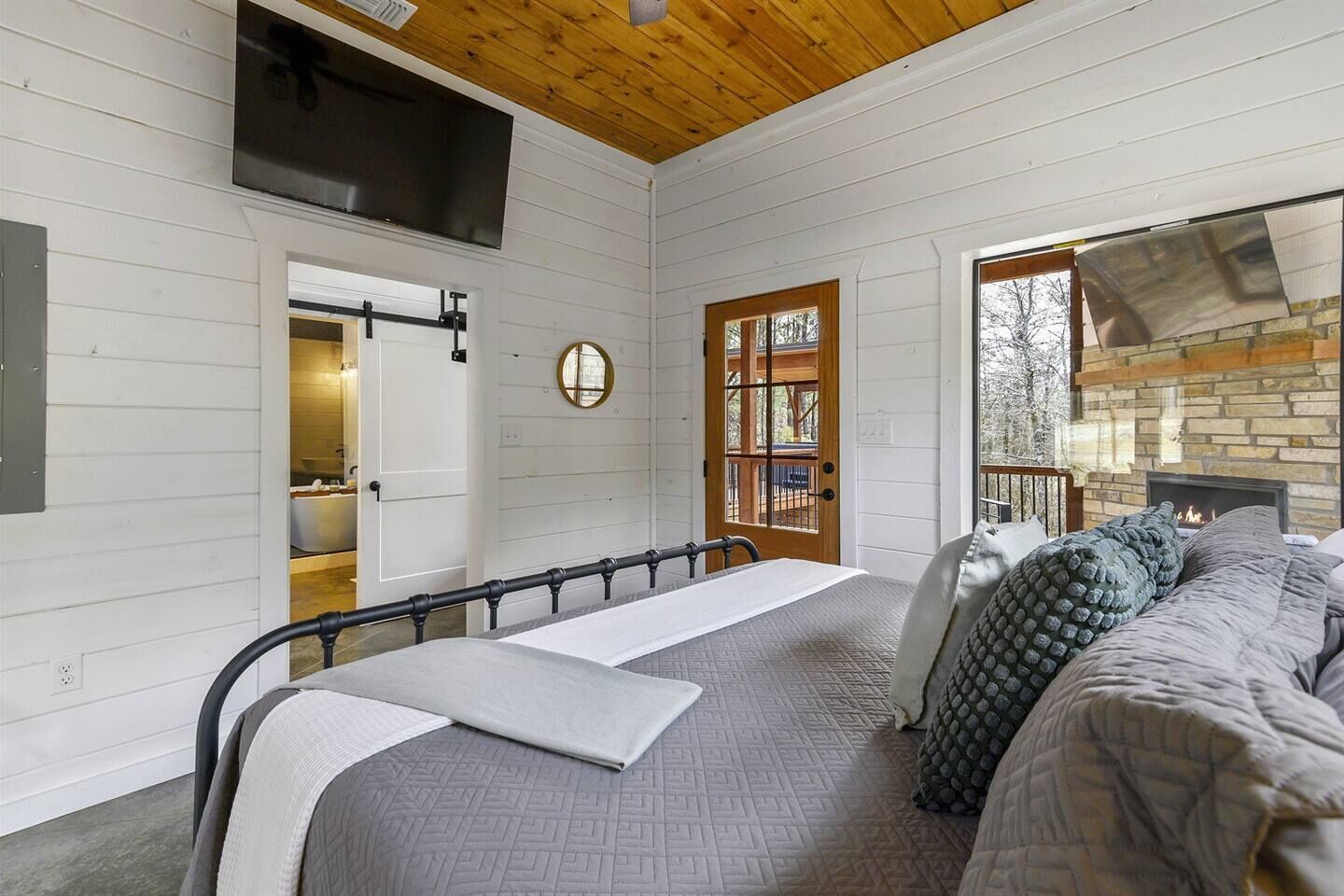 Een slaapkamer met een bed, houten plafond, open haard en uitzicht op de omgeving.