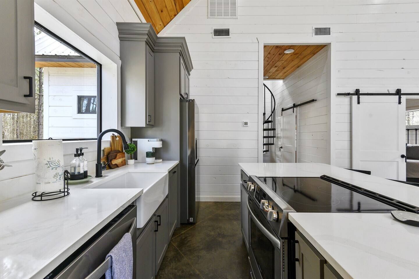 A modern kitchen with white cabinetry, stainless steel appliances, and a wooden ceiling.