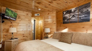 Une chambre rustique en bois, avec un lit, deux tables de chevet, une télévision et un tableau accroché au mur.