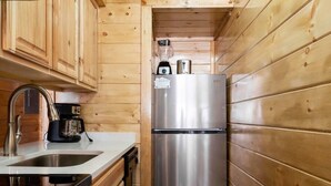 Eine kleine Küche mit Holzwänden, einem Edelstahlkühlschrank, einer Kaffeemaschine und einem Spülbecken.