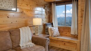 Ein Interieur einer Holzhütte mit einer Couch, einer Lampe und einem Fenster mit Vorhängen.