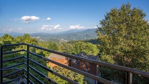 Ein Balkon mit Metallgeländer, der auf eine gebirgige Landschaft mit Bäumen und einem Gebäude blickt.