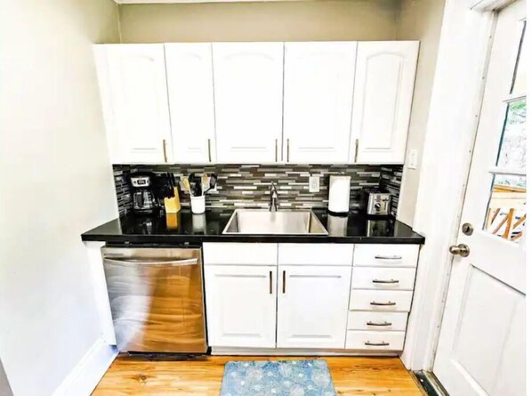 A compact kitchen with white cabinets, a black countertop, and a stainless steel sink.