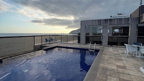 A swimming pool with a view of the sea, a patio area with chairs, and a modern building structure. - Ipanema Flat - Vieira Souto 500  (Rio de Janeiro)