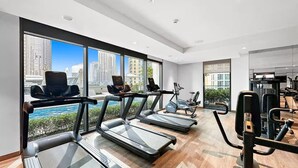 Un gimnasio moderno con cintas de correr, elípticas y máquinas de pesas, con amplias ventanas que ofrecen vistas a la ciudad.