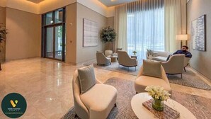 Un espacio habitable amplio con diseño moderno, que cuenta con un ventanal con cortinas translúcidas, una zona de estar con sofás y sillones, y un jarrón decorativo sobre una mesa de centro.