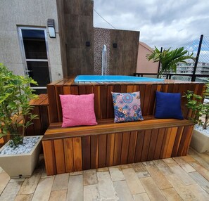 Un banco de madera con tres cojines, una pequeña piscina y un suelo de baldosas de piedra.