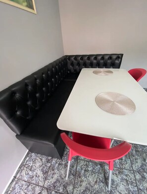 Un rincón con asientos que incluye un sofá de cuero negro y una mesa blanca con sillas rojas.
