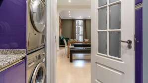 A laundry room with stacked washers and dryers, a dining area with a table and chairs, and a view of the outside through a window.