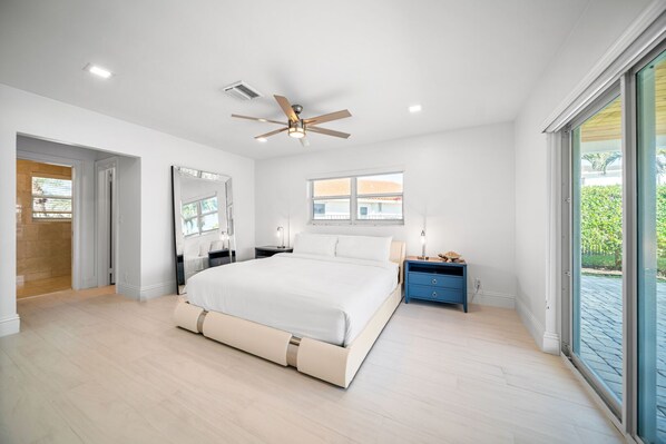 A modern bedroom with a large bed, a ceiling fan, a window, and a nightstand. - 1402 Managed By Brampton Park (Deerfield Beach)