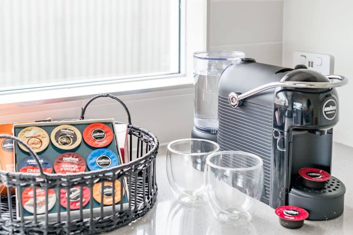 A coffee maker, a basket with coffee pods, and two glasses on a kitchen counter.