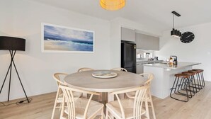 Eine moderne Küche mit Kochinsel, einem Essbereich mit rundem Tisch und Stühlen, einem großen Gemälde an der Wand und einer Pendelleuchte.