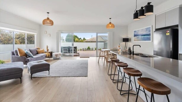 Eine moderne Küche mit einer zentralen Kochinsel, Barhocker und einem Essbereich mit einer Couch und Hocker.