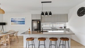Eine moderne Küche mit einer zentralen Kochinsel, Barhocker, einem Essbereich mit Tisch und Stühlen sowie einer Uhr an der Wand.