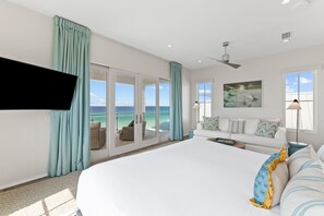 Une chambre avec un grand lit, une télévision, un ventilateur de plafond, un canapé et une vue sur l’océan.
