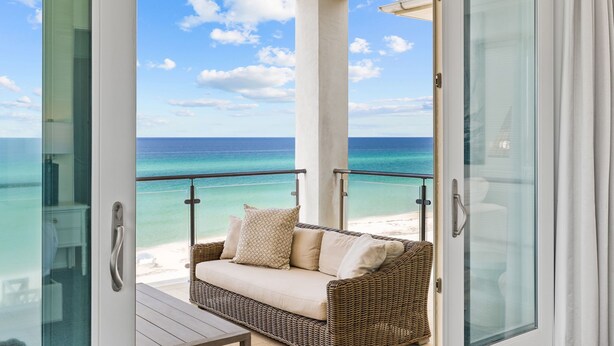A balcony with a wicker sofa, glass doors, and a view of the ocean.