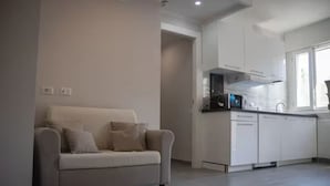 A modern living room with a sofa and a kitchen area with white cabinets and a microwave.