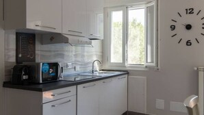 A modern kitchen with white cabinets, a microwave, and a sink. There is a window with a view of greenery outside.