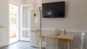 A room with a wooden dining table, white chairs, a white refrigerator, and a mounted television.