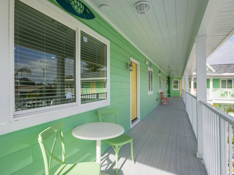 Un edificio verde con un porche cubierto, una mesa y sillas.