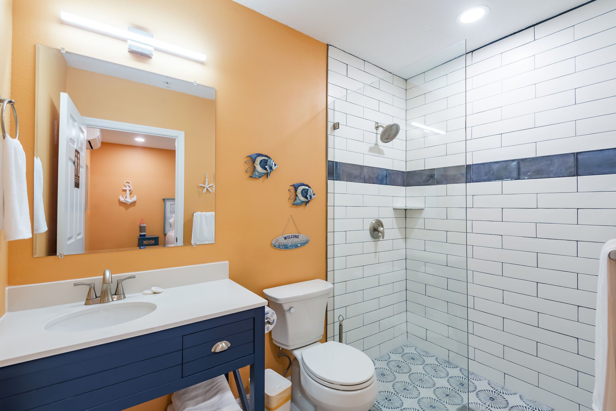 A bathroom with a white sink, blue vanity, white toilet, and a shower area with white and blue tiles.