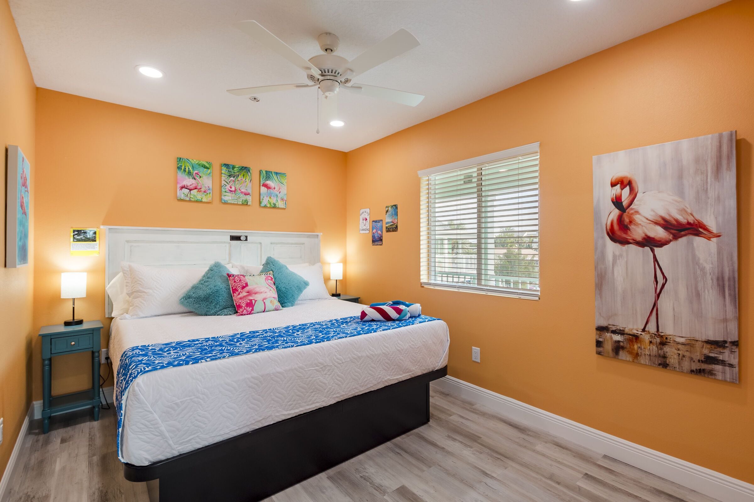 A bedroom with a bed, a ceiling fan, artwork, and a window with blinds.