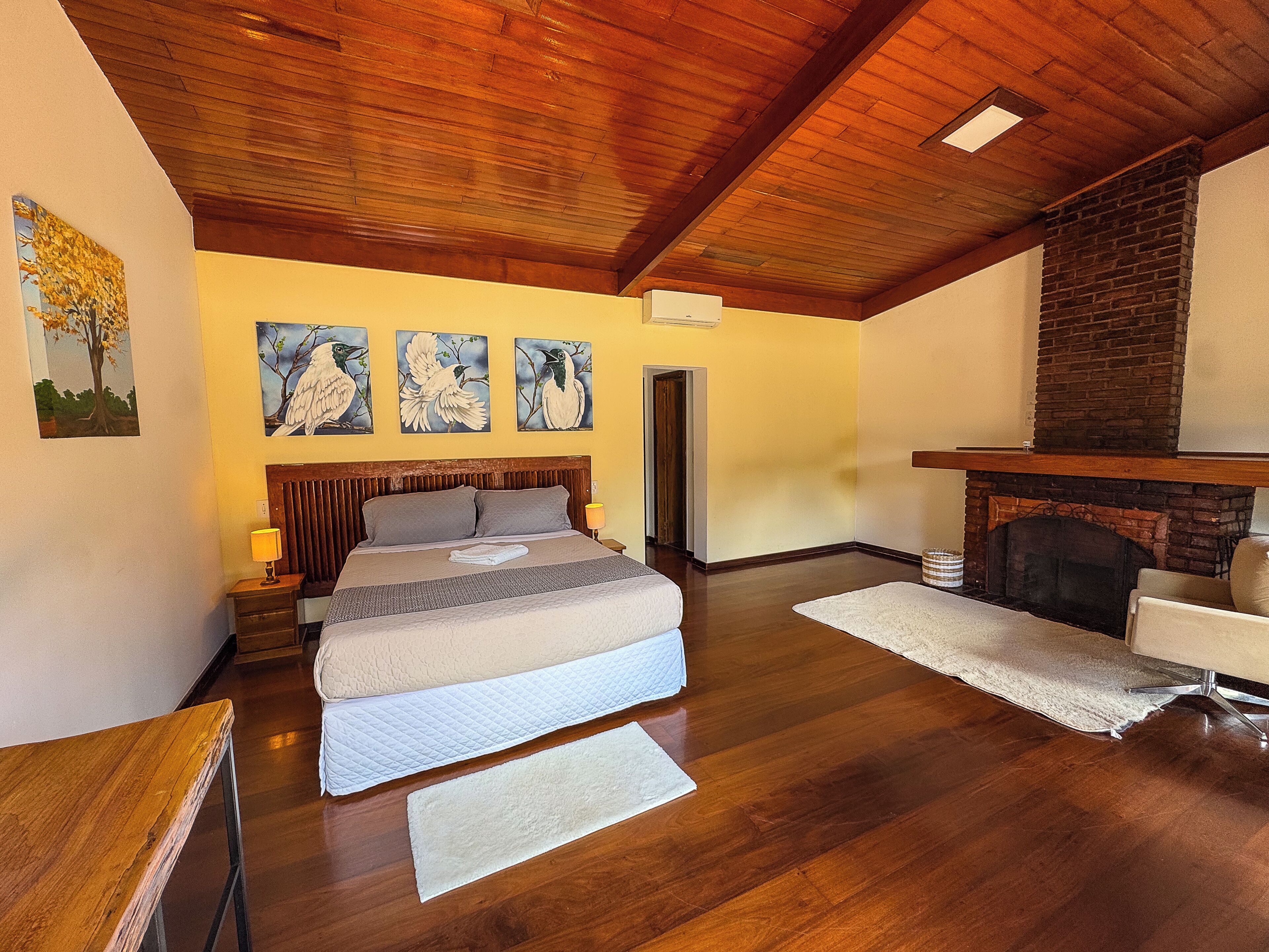 A bedroom with a bed, a fireplace, wooden flooring, and artwork on the wall.