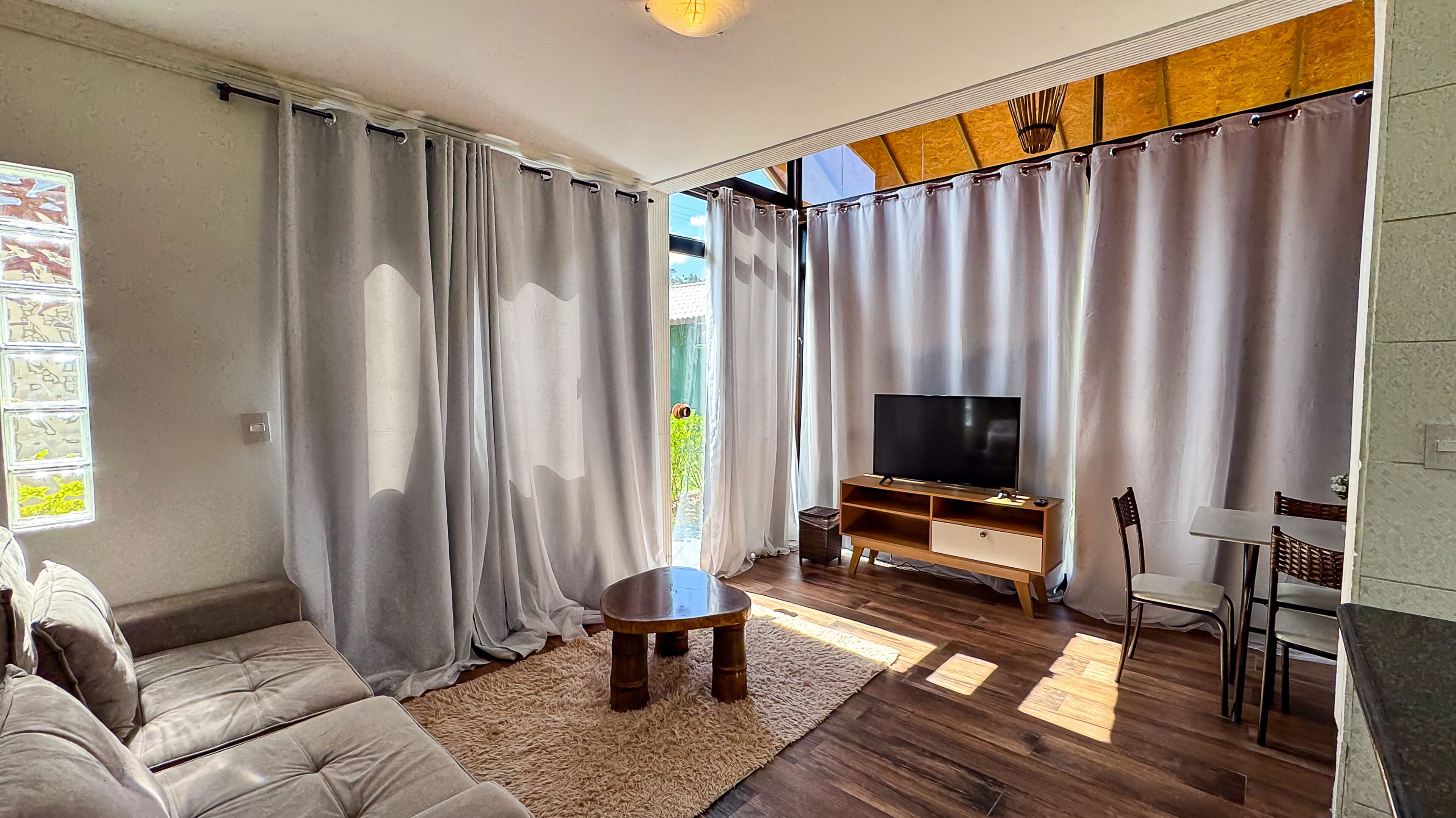 Una sala de estar con sofá, televisión, mueble de entretenimiento de madera y cortinas.