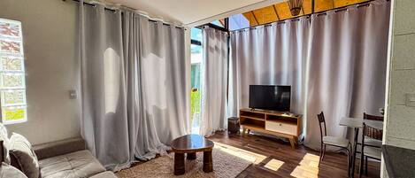 Una sala de estar con sofá, televisión, mueble de entretenimiento de madera y cortinas.