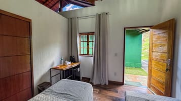 Quarto com cama, escrivaninha, janela com cortinas e porta que dá para o exterior.