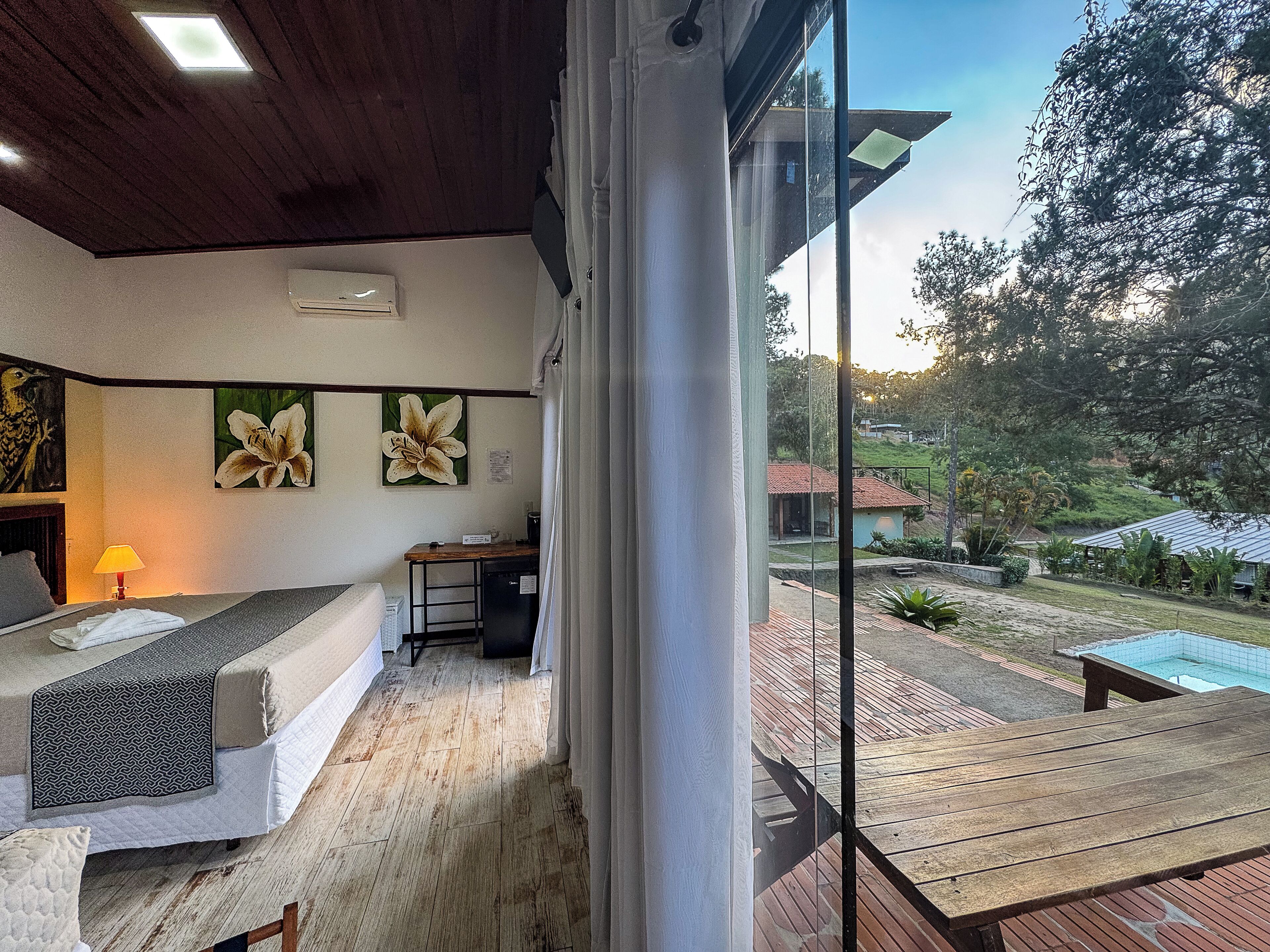 Una habitación con cama, escritorio y vistas a una piscina y vegetación.