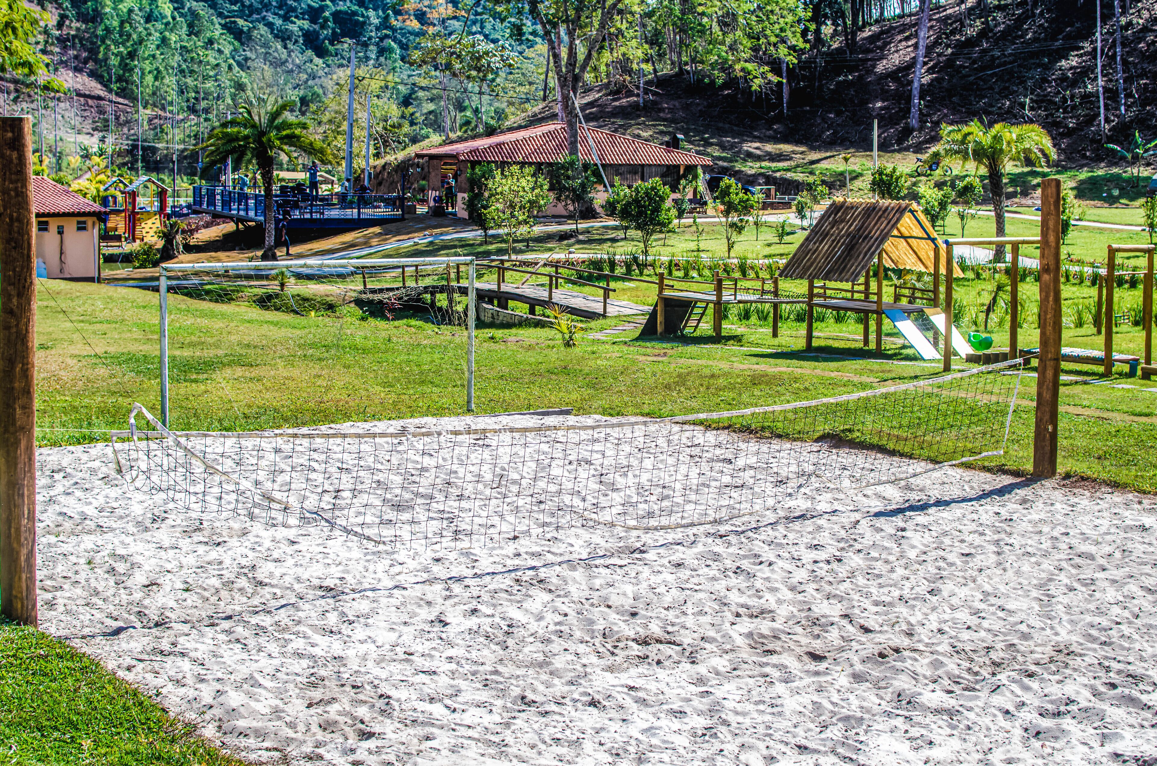Una cancha de voleibol de arena con una red, rodeada por una cerca y diversas estructuras de juego.